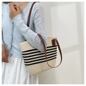 Détail d'un sac cabas en paille tissée avec rayures noires et bretelles en cuir marron
