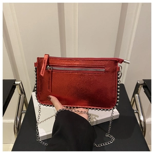Detail of red metallic shoulder bag featuring silver rivets and long chain strap