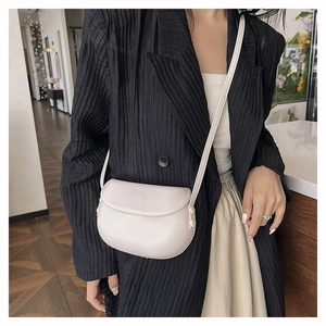 Minimalist ivory saddle shoulder bag shown on model in a stylish indoor setting