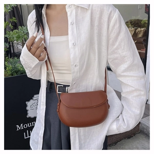 Close-up of a brown leather saddle bag with flap closure worn by a model in a street setting