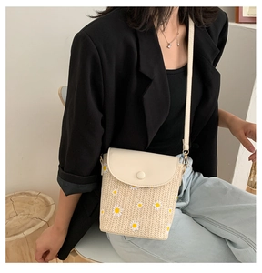 Dettaglio di una borsa a tracolla intrecciata beige con margherite e patta in ecopelle