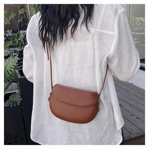 Outdoor shot of a brown leather saddle bag styled as a crossbody on a model back