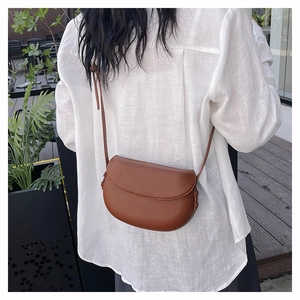 Brown faux leather saddle bag worn by a model in an outdoor garden setting