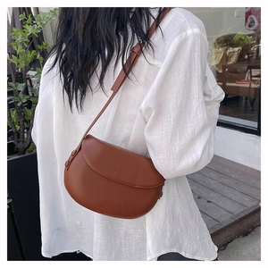Outdoor lifestyle view of a model wearing a brown matte PU leather saddle bag