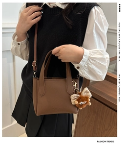 Detail of brown litchi pattern leather handbag with plush monster charm and metal strap buckle