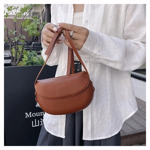 Detail of a brown leather saddle bag featuring a curved flap and side button accents