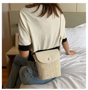 Dettaglio di una borsa a tracolla in paglia intrecciata beige con motivi di margherite