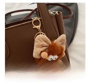 Detail view of a brown plush monster keychain with a cream bow on a leather bag