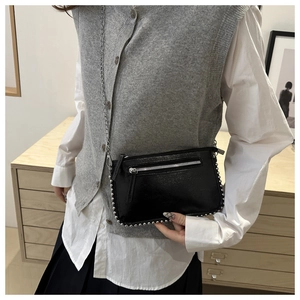 Detail of black patent leather crossbody bag with silver studs and chain strap
