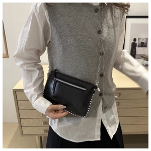 Detail view of a black patent leather crossbody bag with silver rivet trim and metal chain