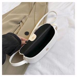 Detail of a creamy white saddle bag showing light gold magnetic clasp and black lining