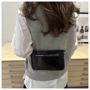 Model wearing a black patent leather crossbody bag with silver studs and chain strap