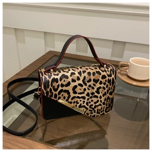 Détail du sac léopard bicolore avec garniture dorée posé sur une table en bois