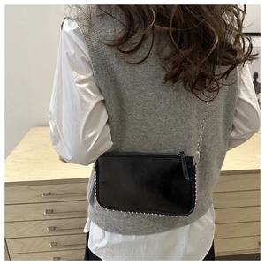 Detail of black glossy leather crossbody bag with silver studs and chain strap on a model