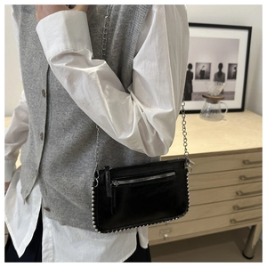 Detail of black patent leather crossbody bag with silver studs and chain strap