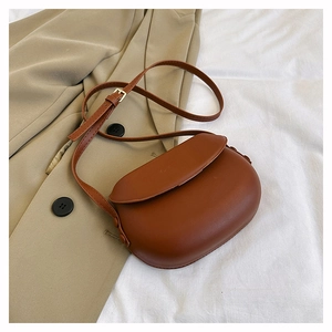 Top view of a vintage brown saddle bag on a beige blazer and white pleated fabric