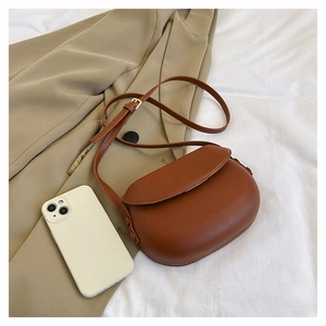 Close-up of brown saddle bag with adjustable strap and metal buckle on beige blazer