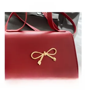 Gros plan sur un sac en cuir rouge avec un nœud décoratif en métal doré sur le rabat