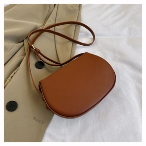 Close-up of brown faux leather saddle bag with adjustable strap and gold buckle