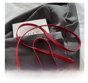 Gros plan d'une bandoulière en cuir rouge avec boucle dorée en nœud sur une veste grise