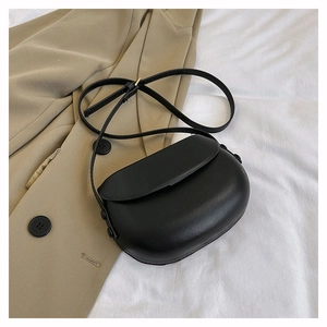 Detail of a minimalist black leather saddle bag styled with a beige blazer on white fabric