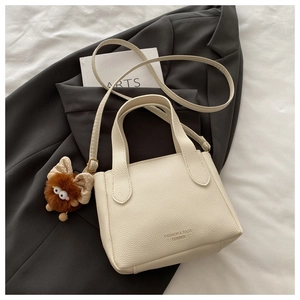 Dettaglio di una borsa a secchiello in pelle crema con ciondolo a mostro di peluche marrone