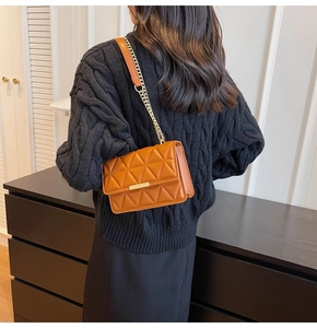Detail of caramel quilted crossbody bag with gold buckle and chain strap on black sweater