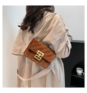 Sac bandoulière en velours marron avec chaîne dorée porté avec un trench-coat beige
