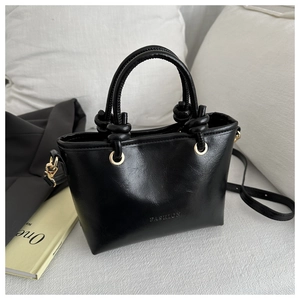 Détail du sac à main noir en cuir avec lettrage fashion et nœuds décoratifs sur l'anse