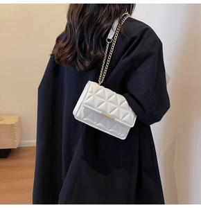Close-up of white quilted crossbody bag with gold chain strap worn on black blazer