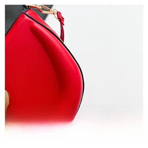 Detail view of red glossy leather saddle bag with golden lobster clasp and fine stitching