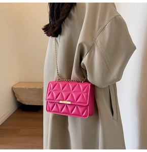 Detailed view of magenta quilted handbag with gold chain strap and metallic clasp on coat