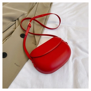Detail of red matte leather saddle bag on white fabric with casual blazer backdrop