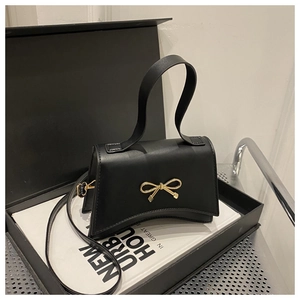 Detail of black matte leather shoulder bag featuring a gold bow buckle and curved base