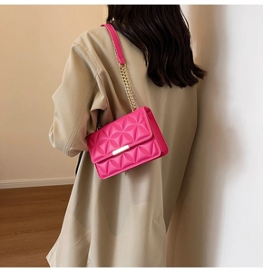Detail of rose red quilted crossbody bag with gold chain strap on beige coat