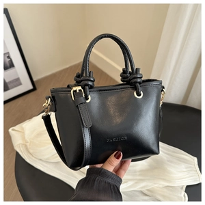 Détail d'un sac seau en cuir noir avec anneaux dorés et poignée à nœuds élégante