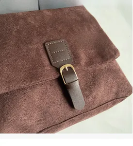 Detailed close-up of golden metal buckle on a brown suede flap crossbody bag