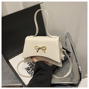 Detail of a cream trapezoid handbag with a golden bow clasp and leather handle straps