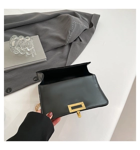 Gros plan du sac bandoulière en velours noir avec chaîne dorée et fermoir rotatif rectangulaire