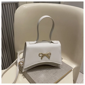 Detail of white PU leather crossbody bag featuring a golden metal bow accessory