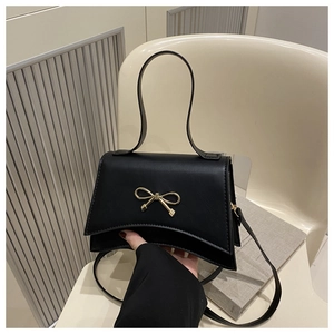 Detail of black bow square bag showing curved bottom design and golden metallic bow