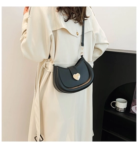Close-up of black matte leather saddle bag with a polished gold heart-shaped metal buckle