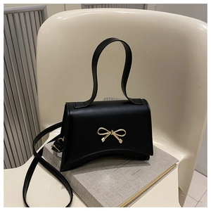 Detail of black faux leather handbag featuring a golden metal bow clasp on a curved base