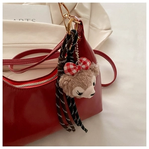 Close-up of a glossy red patent leather underarm bag with a cute bear charm and woven strap