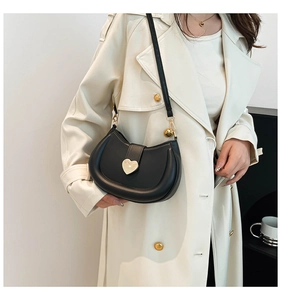 Close-up of black crescent shoulder bag with a gold heart-shaped metal buckle detail