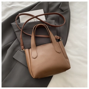 Detail showing brown lychee grain leather texture and metallic hardware on bucket bag