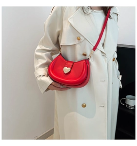 Detail of red leather saddle bag with gold heart clasp worn over a beige trench coat