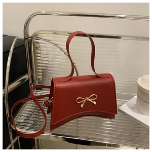 Macro detail of red leather bag showing the golden metal bow clasp and smooth texture