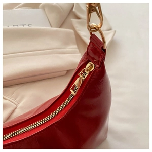 Detail of red glossy leather shoulder bag featuring golden metal zipper and stitching