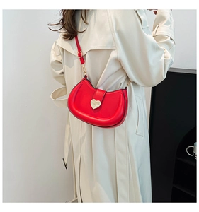 Detail of red crescent leather saddle bag with gold heart clasp worn over white coat